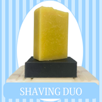 Blue Striped Background with White Oval Frame of a set of soaps sitting on a  soap dish. One is a black Deep Clean Soap Bar, the other is a White colored Shaving Bar. The text reads Shaving Duo.