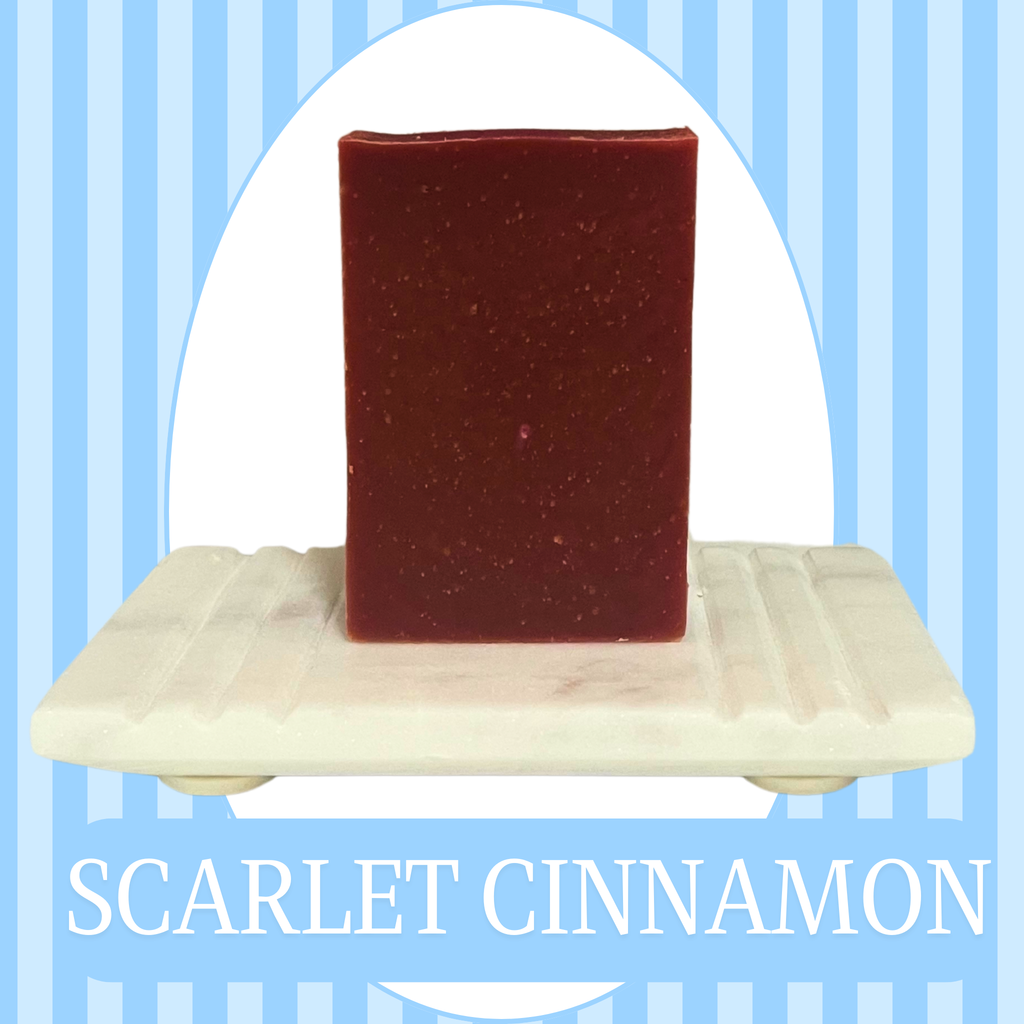 Blue striped background with a white oval frame around a sisal bag holding a blue bar soap. The text reads Scarlet Cinnamon.